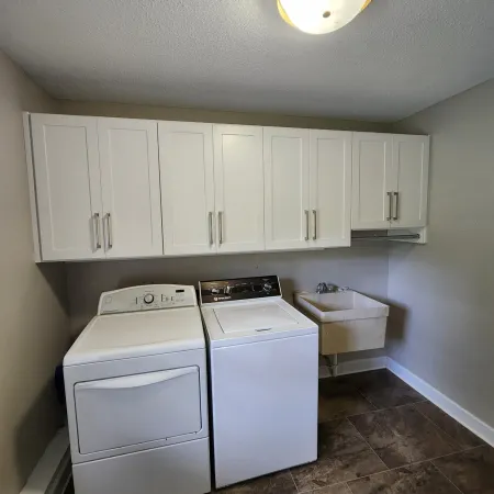 Laundry room with white washer, dryer, upper cabinets, utility sink, and ceiling light on tiled floor.