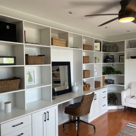 White built-in shelves with wicker baskets and office desk with rolling chair in bright hardwood floor room