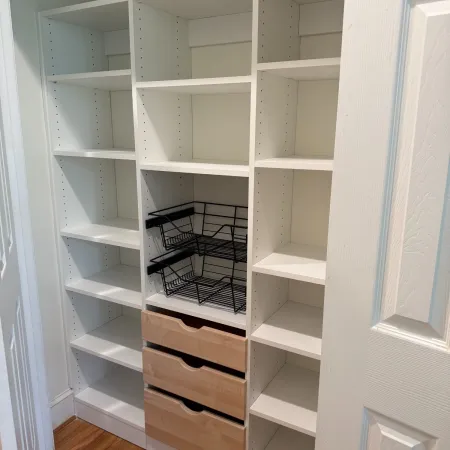 White wooden cubby shelves with black wire baskets and three wooden drawers on a hardwood floor.