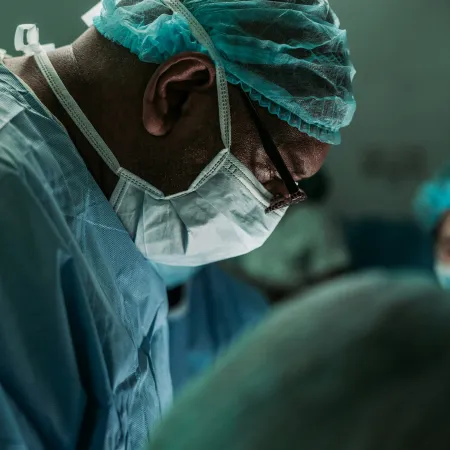 Surgeon wearing protective mask and cap focused on surgery in a sterile operating room environment.