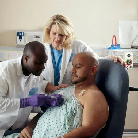 Two medical professionals attending to a seated male patient with an IV catheter in a clinical setting.