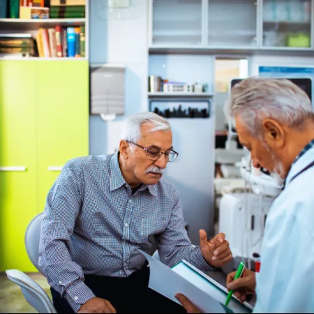 Senior man consulting with doctor in a medical office discussing test results and health checkup.