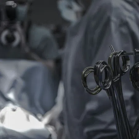 Close-up of surgical instruments with surgeons operating in the background under focused light in an operating room.
