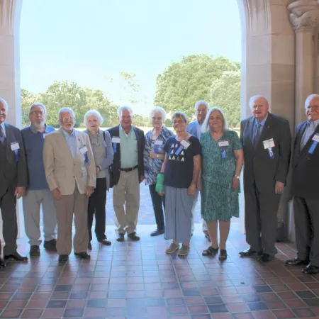Group of senior adults standing together in a sunlit archway during a formal gathering or reunion.