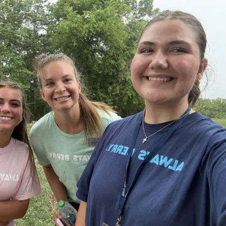 Three smiling young women outdoors wearing pastel shirts with 'ALWAYS BERRY' text, standing in front of green trees.