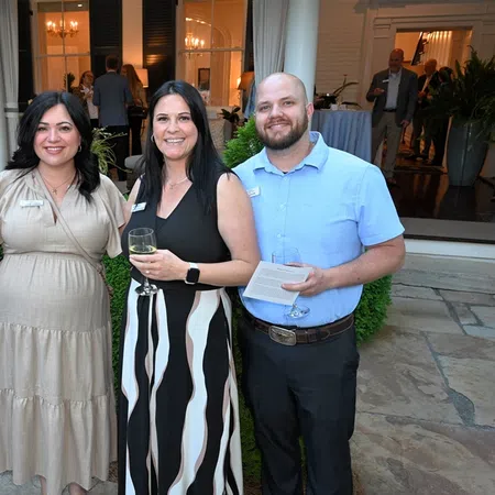 Four adults posing outside a building, smiling, with plants and flowers in the background during an event.