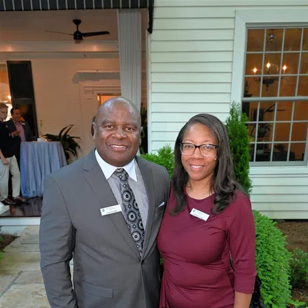 Man in gray suit and woman in burgundy dress smiling outdoors at formal event near building.