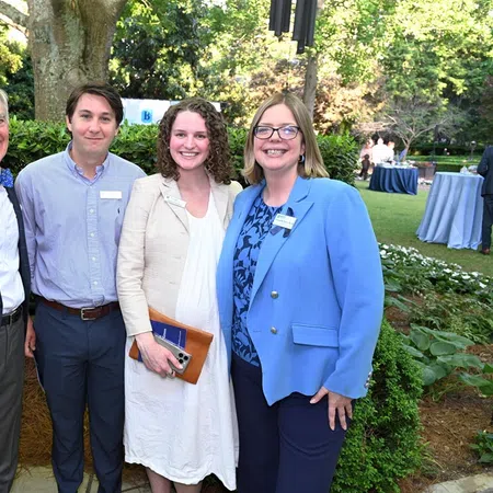 Four professionals posing outdoors in business casual attire at a garden event with greenery and tables in the background