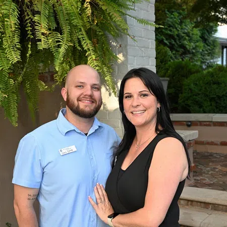 Smiling couple standing outdoors near brick stairs and greenery, posing for a photo together.