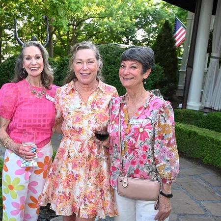 Four women in colorful dresses smiling outdoors at a social event during the daytime.