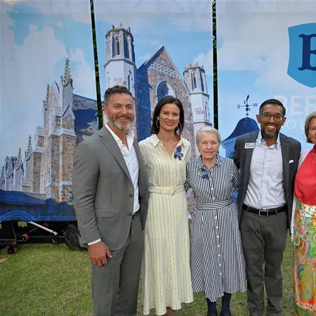 Group of six professionally dressed people posing outdoors in front of Berry College banners with campus buildings.