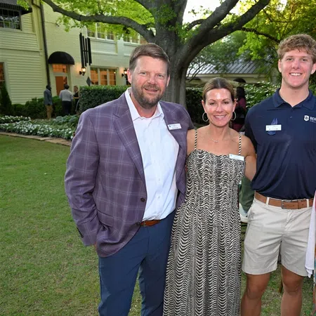 Four people smiling outdoors at a garden event, dressed in summer attire with trees and a house in the background