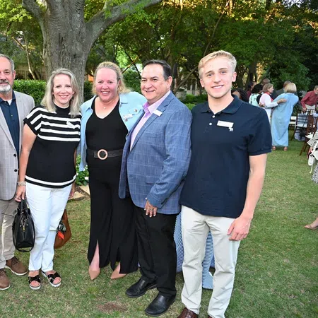 Group of six people smiling and posing outdoors in a garden setting during a social event.