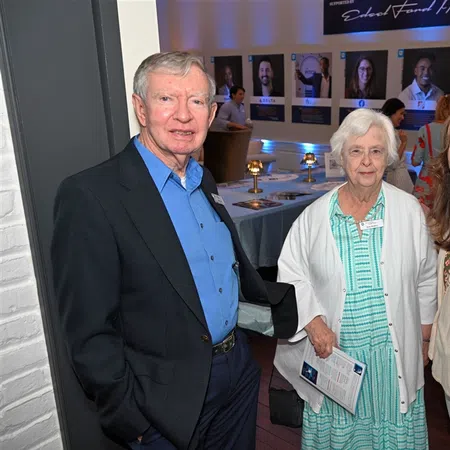 Three adults smiling at a social event with informational displays and guests in the background indoors.