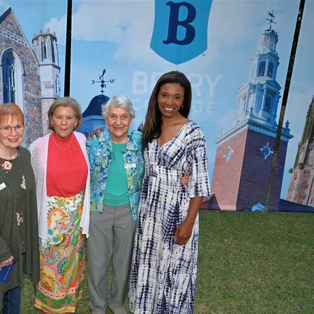 Four women smiling and posing outdoors in front of a Berry College backdrop with historic buildings.