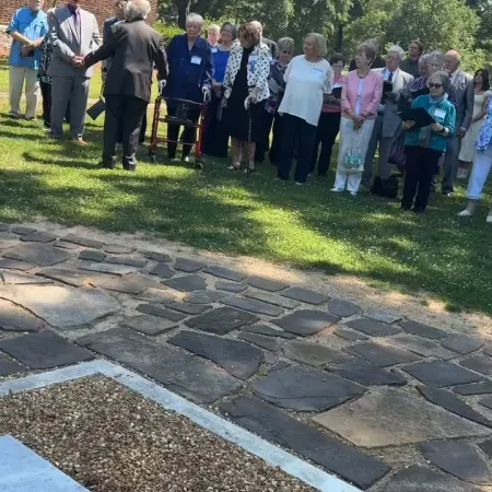 Group of elderly people gathered outdoors near a brick building on a sunny day.