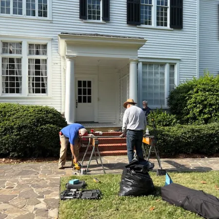 Two men working on home maintenance outside a white house with large windows and columns.