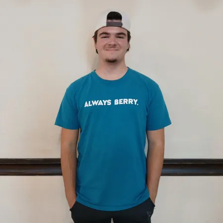 Young man wearing a white backwards cap and blue t-shirt with Always Berry text standing against plain wall