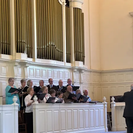Choir group performing in a church with large organ pipes and a conductor leading from the front.