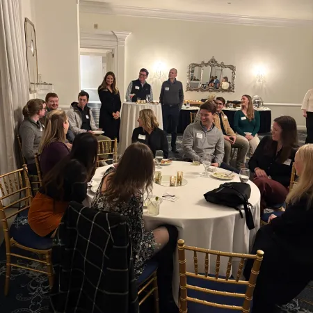 Group of people seated and standing around a dining table in a formal event room with elegant decor.