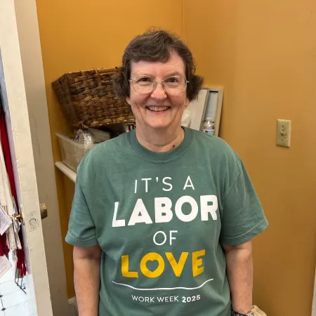 Smiling woman wearing green shirt that says It's a Labor of Love Work Week 2025 in a room with mustard walls.