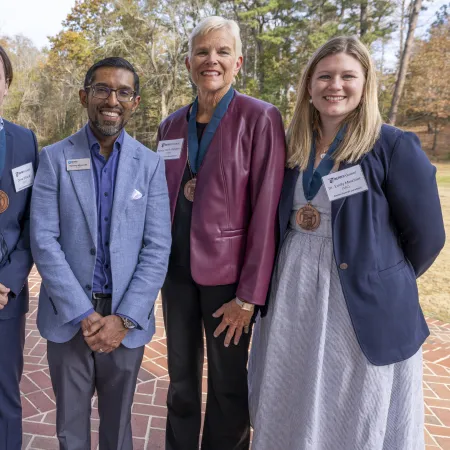 Five smiling professionals wearing name tags and medals standing outdoors on brick pavement during daytime