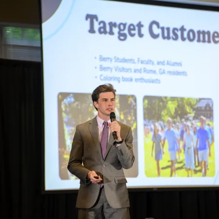 Man in suit presenting Target Customer slide to an audience in a conference setting.
