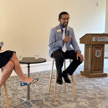 Two professionals seated on stools engaged in a discussion with microphones in a conference setting at Berry College.