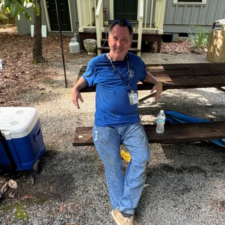 Man in blue shirt and jeans relaxing on an outdoor wooden bench surrounded by gravel and greenery.