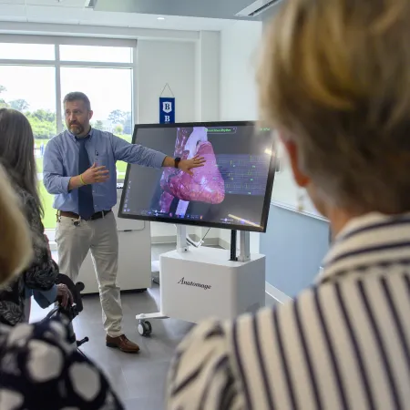 Person giving a medical presentation on a digital lung model to an audience in a bright classroom.