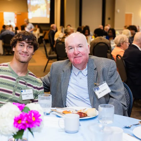 a couple of men sitting at a table with food and drinks