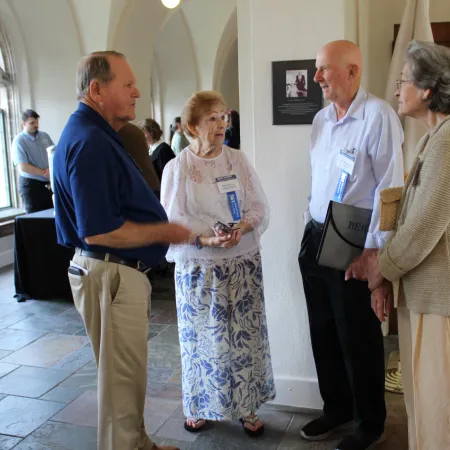Group of elderly people engaged in conversation inside a building with tiled floor and arched ceiling.