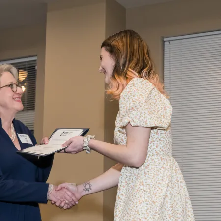 Woman in navy dress handing certificate while shaking hands with woman in floral dress at event