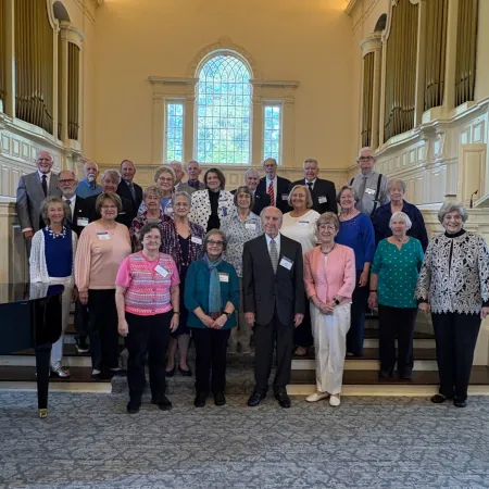 Group portrait of adults standing together inside a historic building with large windows and ornate architecture