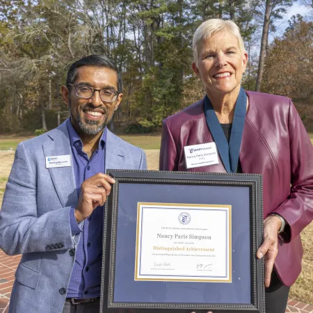 Two people outdoors holding a framed Distinguished Achievement award certificate with trees in background.