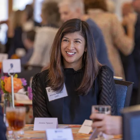 Smiling woman with name tag seated at a table during a formal social or networking event.