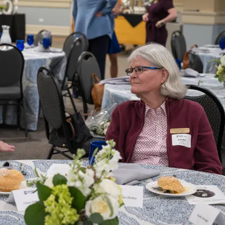 Two women engaged in conversation at a round table with food and floral centerpiece in a formal dining setting