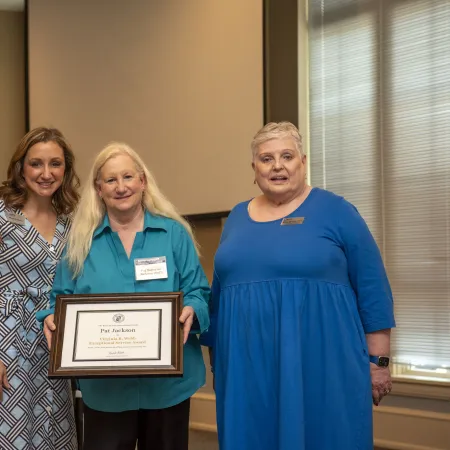 Group of four adults posing indoors with one holding a framed award certificate beside a grand piano
