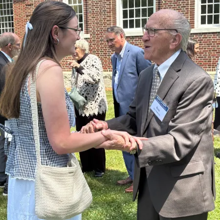 Older man in suit shaking hands with young woman in summer dress outside brick building on sunny day