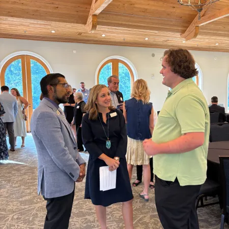 People dressed in business casual attire networking in a bright room with wooden ceiling and large arched windows.