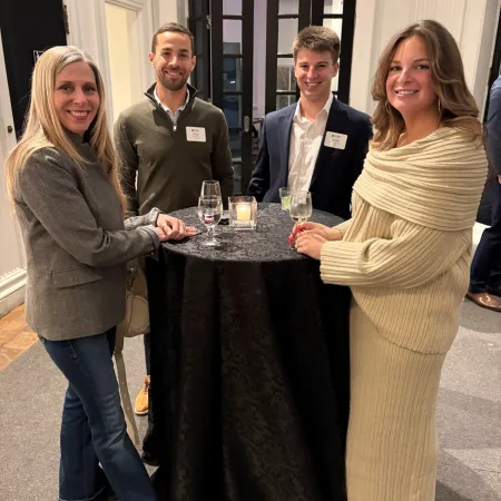 Four people smiling around a high-top table with drinks in a social indoor setting.