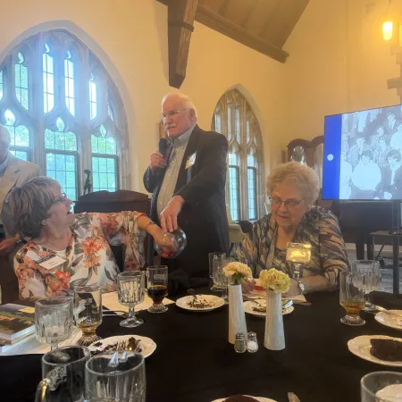 Elderly people enjoying a meal and conversation with wine in a cozy room with stained glass windows.