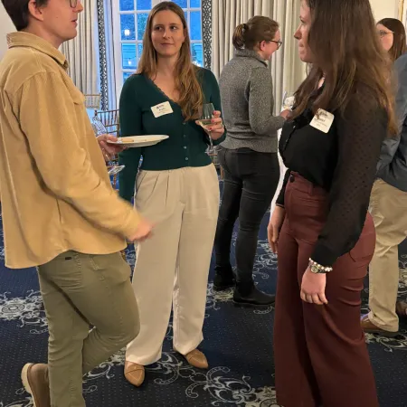 Group of people socializing indoors at a networking event with drinks and name tags on a patterned carpet.
