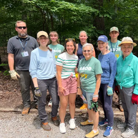 Group of volunteers posing outdoors in a wooded area during a community labor of love project on a sunny day