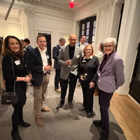 Group of six people posing and smiling in a well-lit indoor space with ornate white walls and wood flooring.