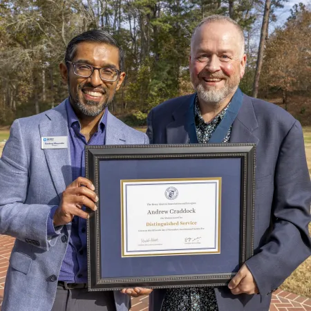 Two men outdoors smiling while holding a framed certificate of distinguished service award.