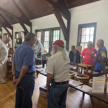 Group of people interacting and examining auction items in a large room with wooden beams and tables.