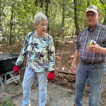 Older couple in casual clothes standing on a forest trail surrounded by green trees during daytime