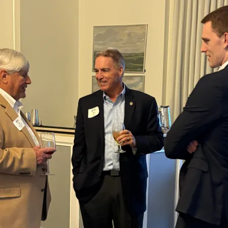 Three men in business attire socializing and holding drinks at an indoor networking event.