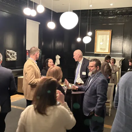 Professionally dressed people mingling and conversing in an elegant room with black walls and modern spherical lights.